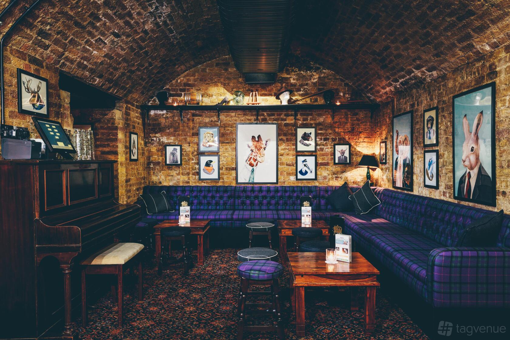 A cocktail bar with exposed brick vaulted ceilings, plaid upholstered sofas, and eclectic framed art at The Cocktail Club Monument.