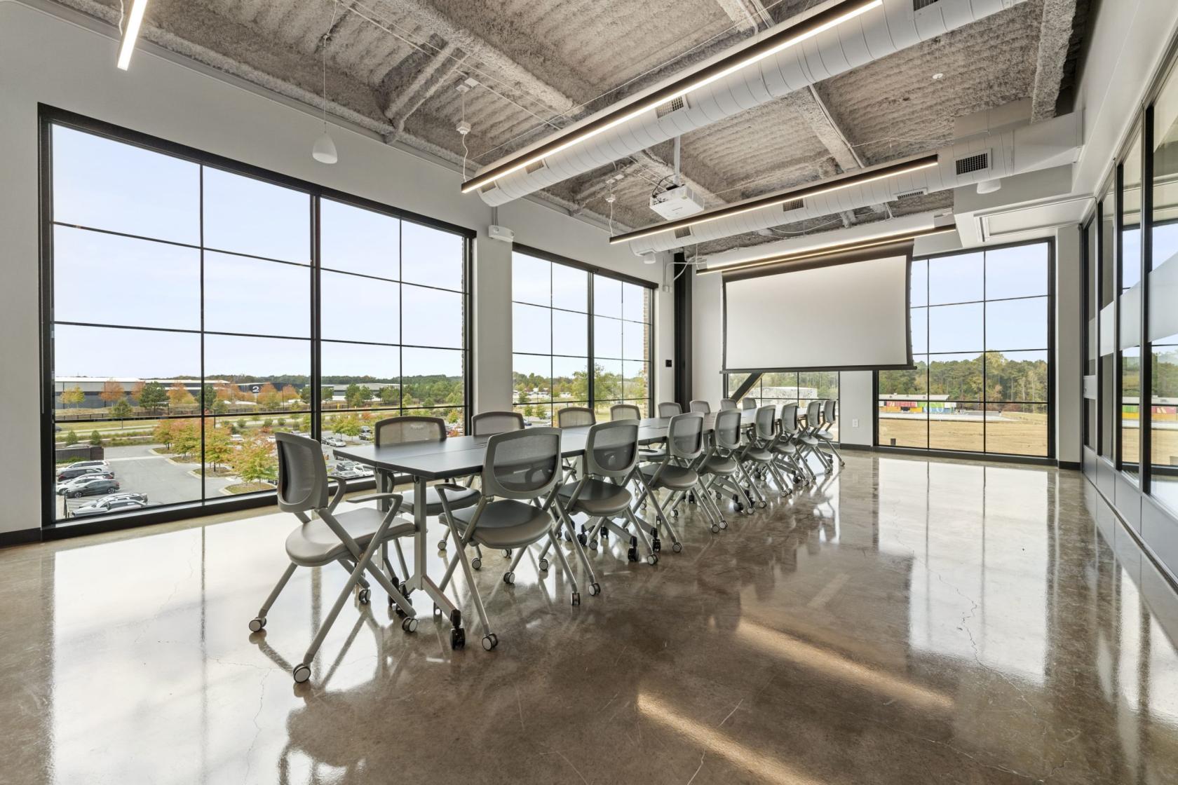 A training room with floor-to-ceiling windows, polished concrete floors, and a projection screen at ROAM AT TRILITH.
