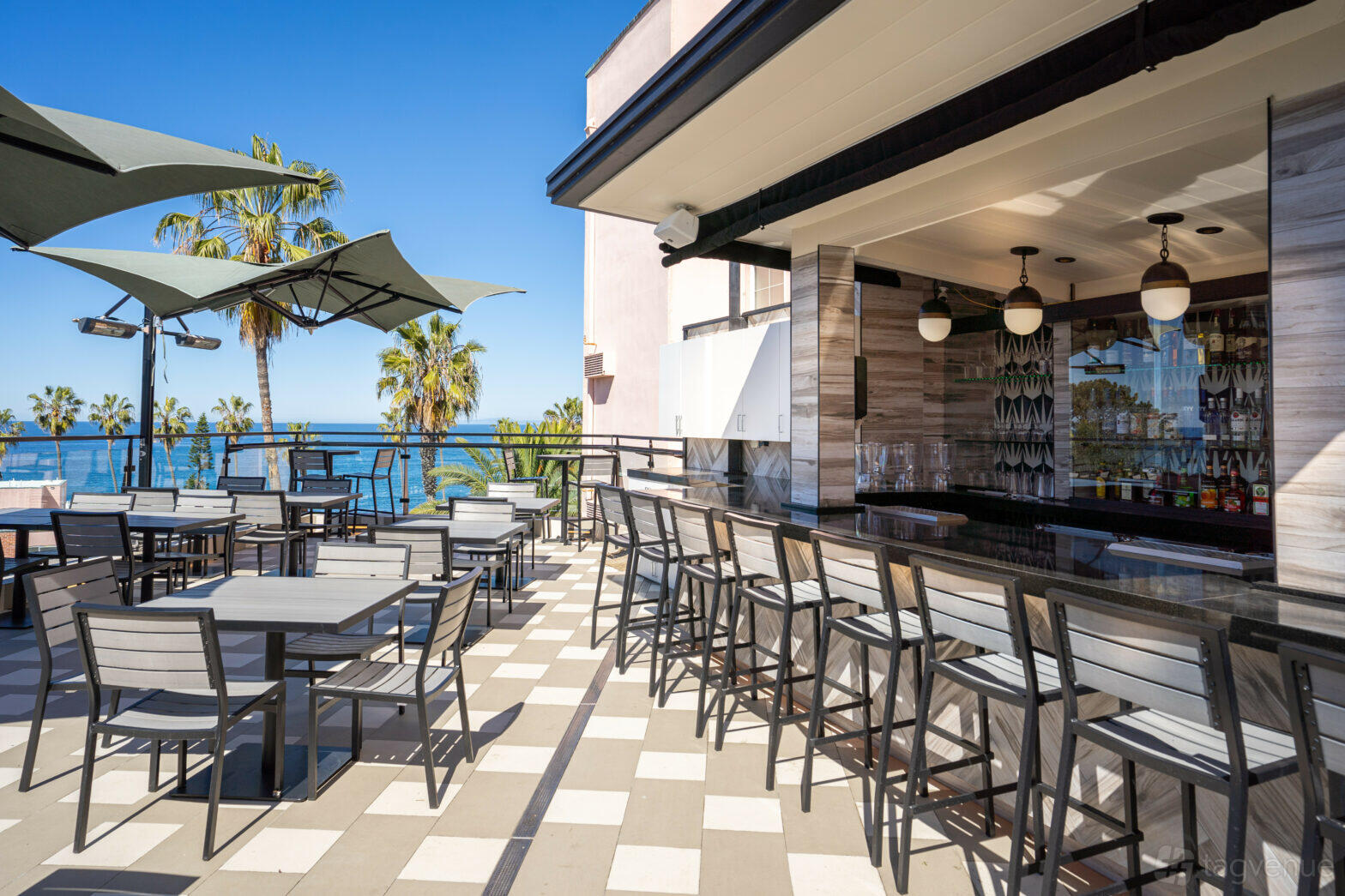 A hotel terrace with ocean views, shaded outdoor seating, and a sleek bar at Cormorant Boutique Hotel - La Jolla.