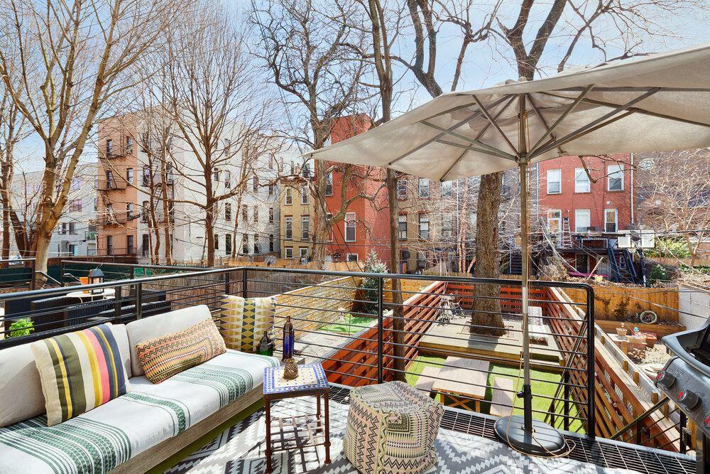 An apartment patio with cushioned seating, patterned pillows, a large umbrella, and views of a fenced backyard at Casa Diamond.