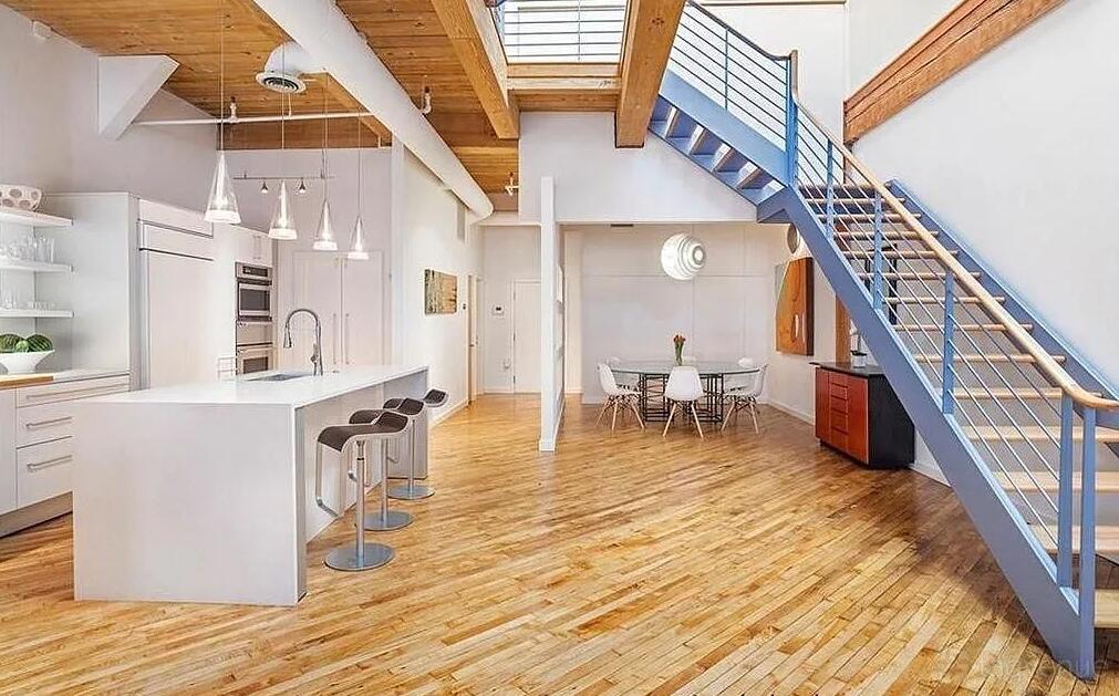 A penthouse with an open kitchen, pendant lights, wooden floors, and a metal staircase at Penthouse Property.