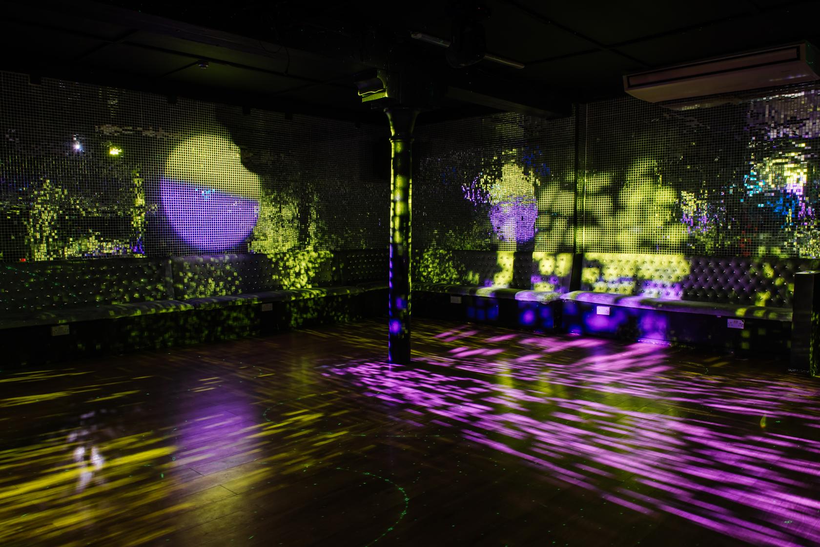An event space in a nightclub with mirrored walls, tufted banquette seating, and purple-yellow light effects at La Pollera Colora.