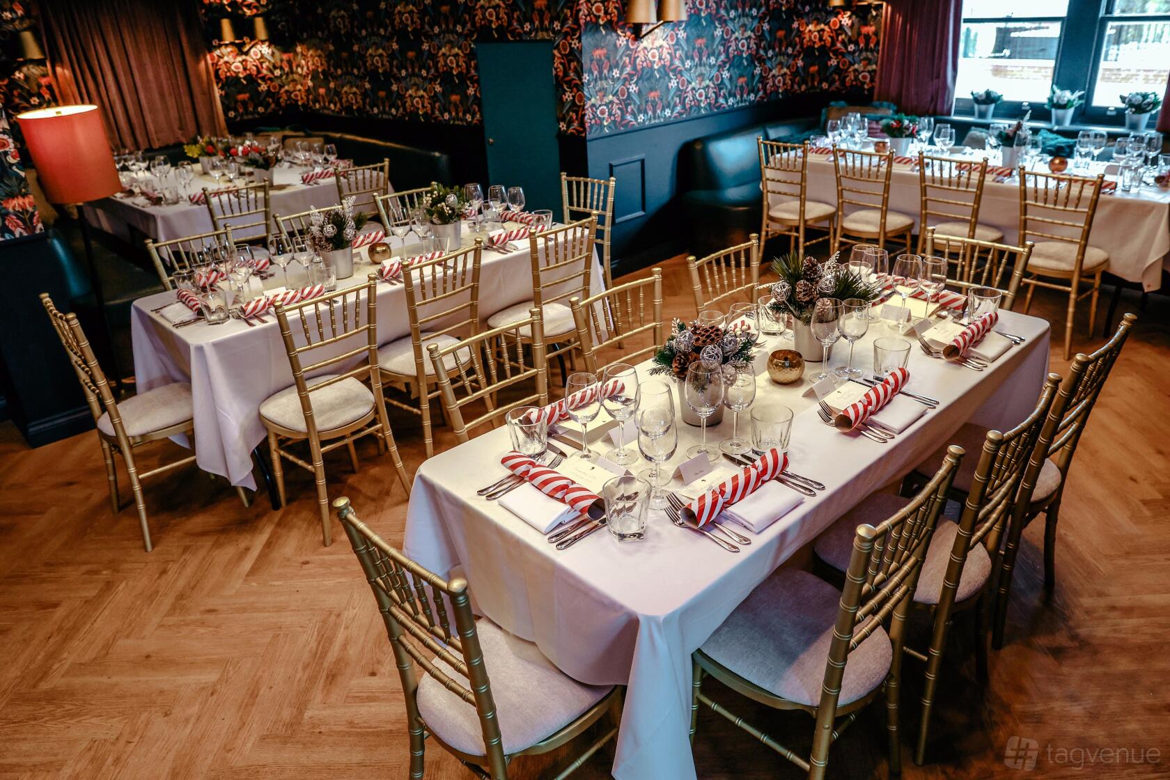 An event space in a cocktail bar with banquet tables, gold chairs, floral centerpieces, and patterned wallpaper at Albert's at Beaufort House.