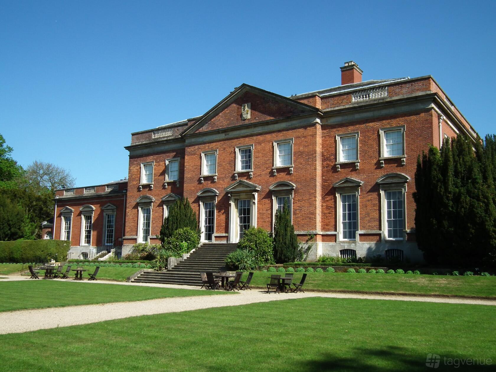 A historic hall with red brick facade, tall windows, and manicured lawn seating at Kelmarsh Hall.