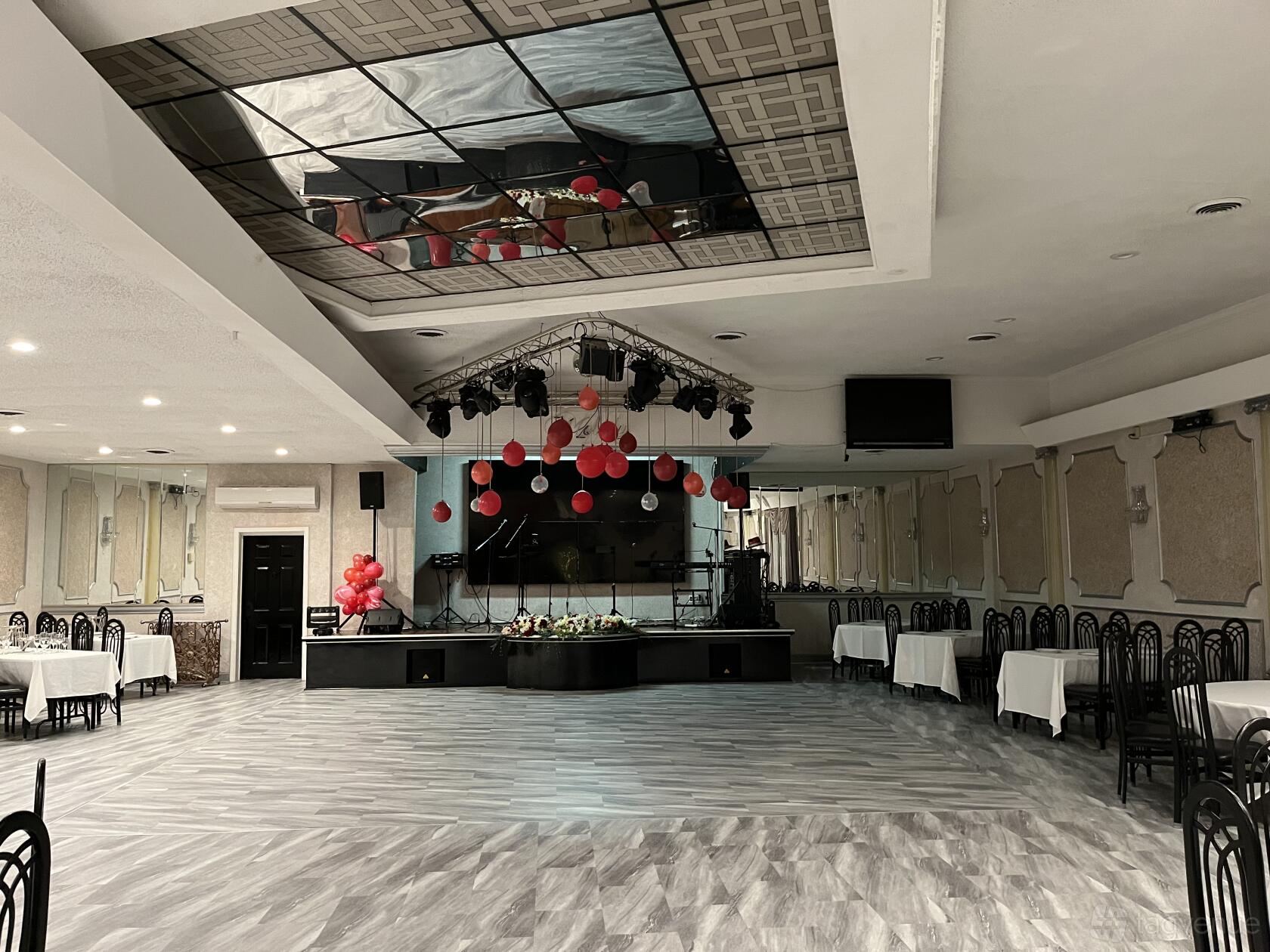 A hall with a mirrored ceiling, gray patterned flooring, and tables with white linens at Melody.