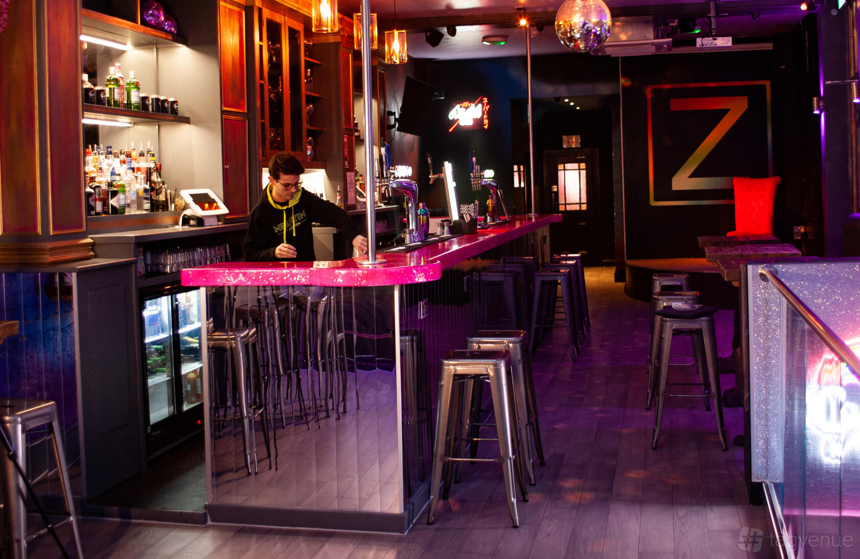 A cocktail bar in a nightclub with a neon-lit counter, mirrored shelves, and metal barstools at ZODIAC Karaoke Bar & Club.