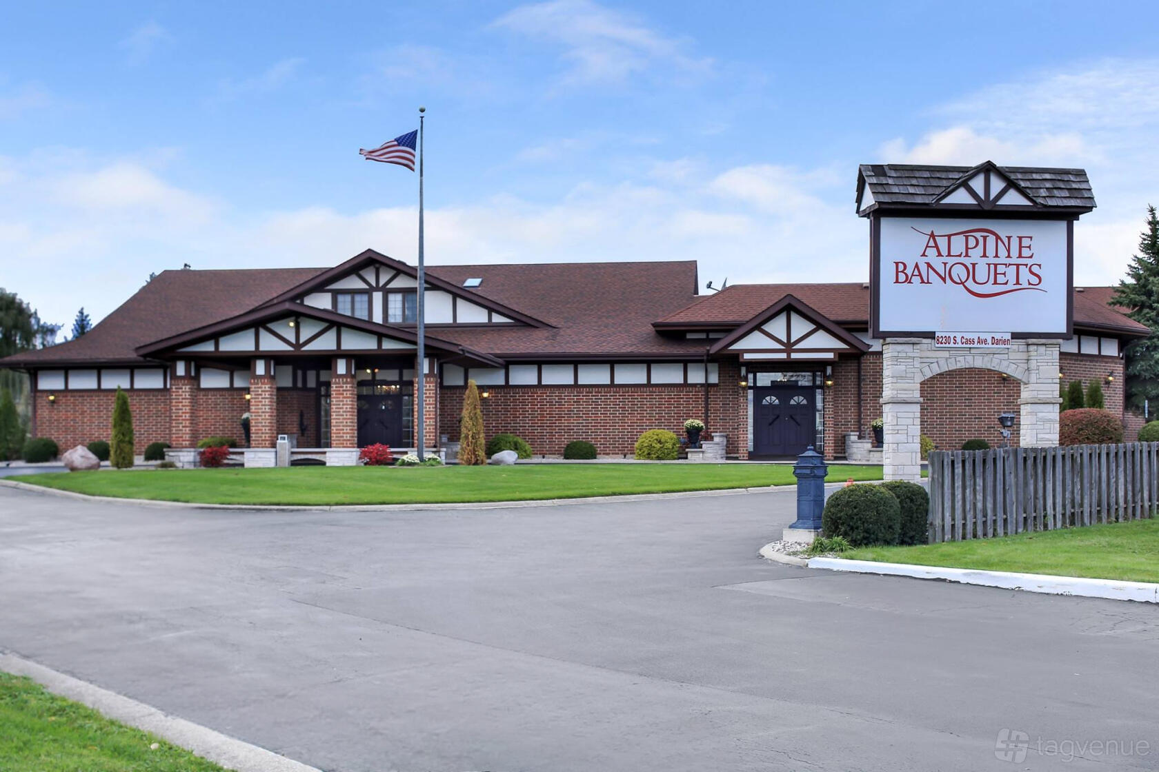 A brick event venue with a peaked roof, central entrance, and large roadside sign at Alpine Banquets.