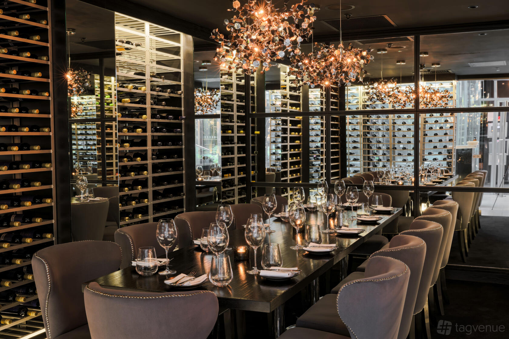 A restaurant dining room with glass wine walls, dark wood table, and chandeliers at Gaucho Broadgate.