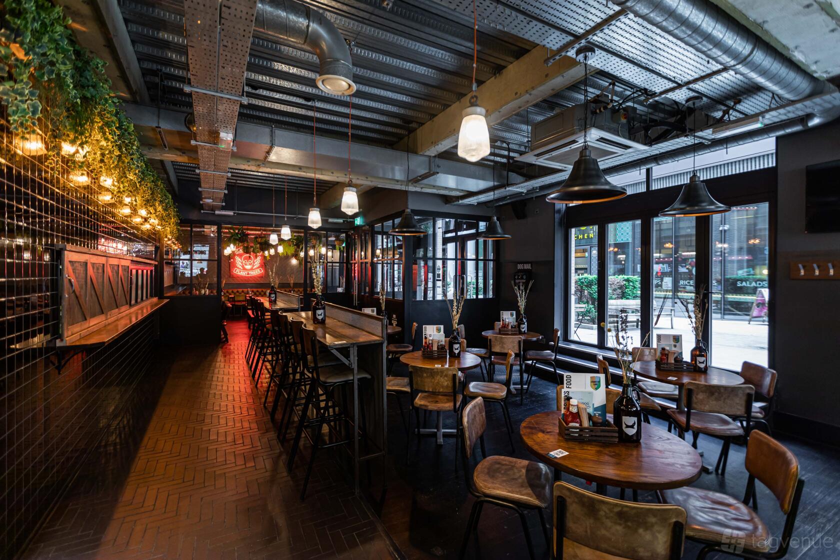 An event space in a restaurant with round wooden tables, industrial lighting, and large windows at BrewDog Chancery Lane.