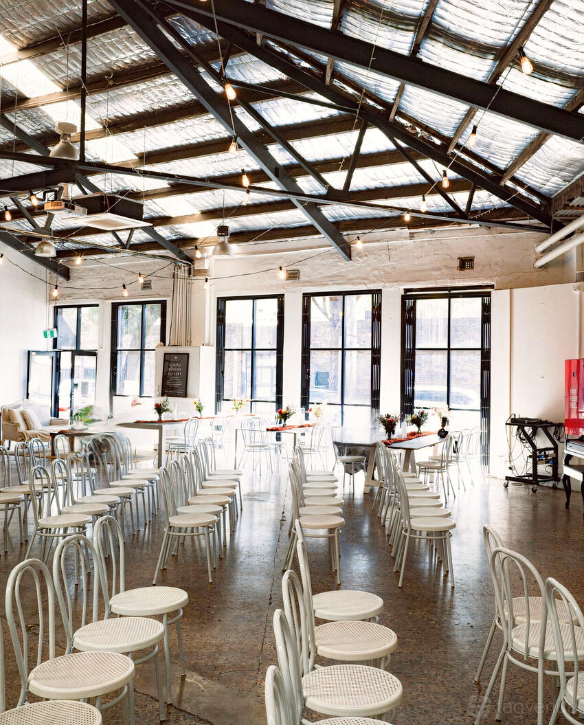 A cafe with metal chairs, exposed beams, large windows, and small floral centerpieces at The Freedom Hub.