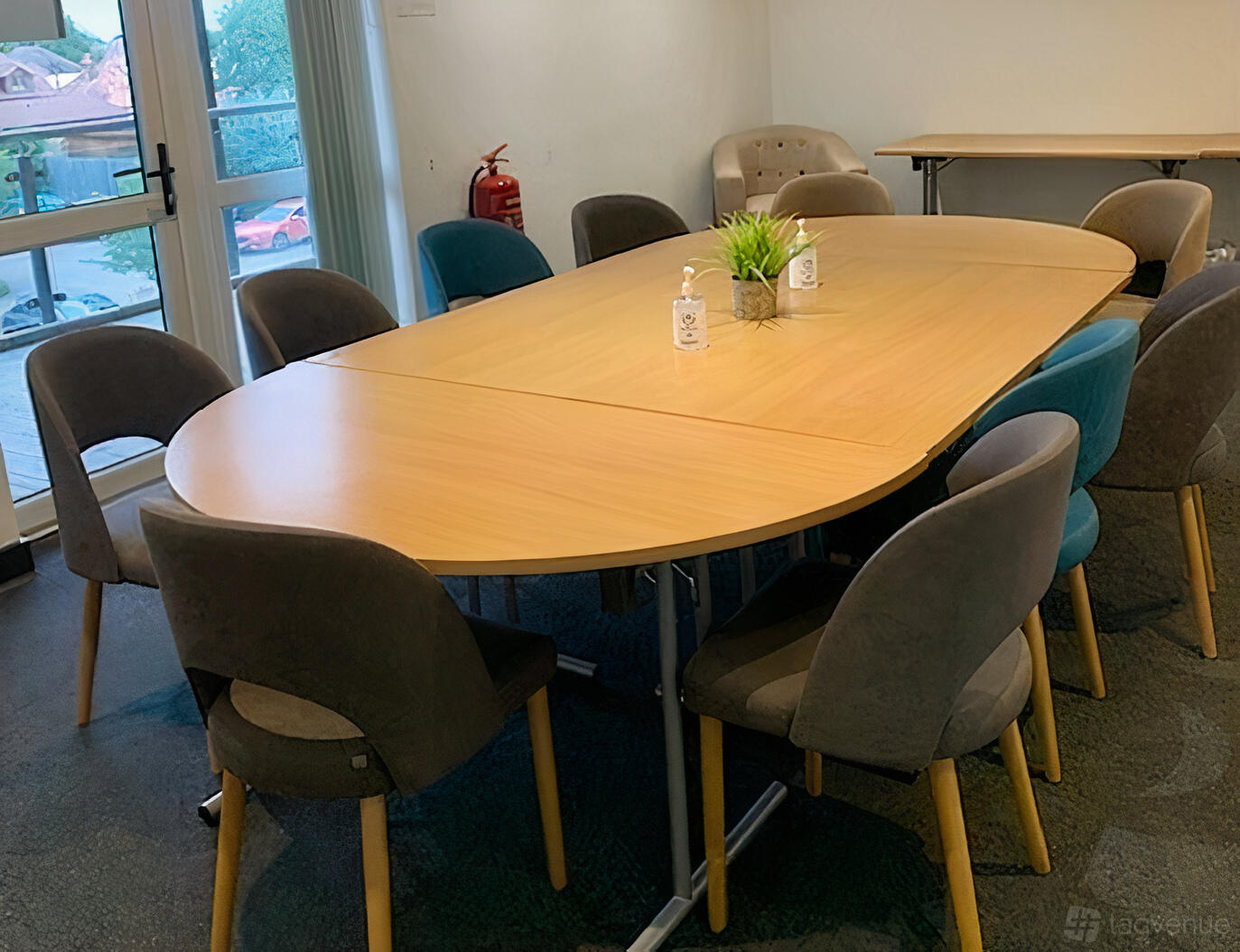 A meeting room with an oval wooden table, upholstered chairs, large windows, and a potted plant at The Thames Club Health Club.