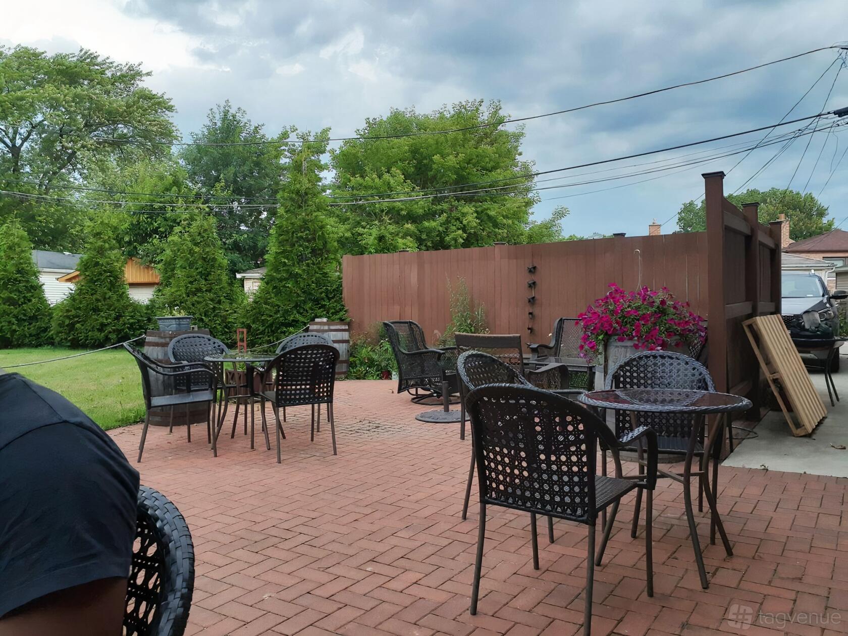 An outdoor patio with black metal tables and chairs, brick flooring, and potted flowers at Wild Blossom Meadery & Winery.