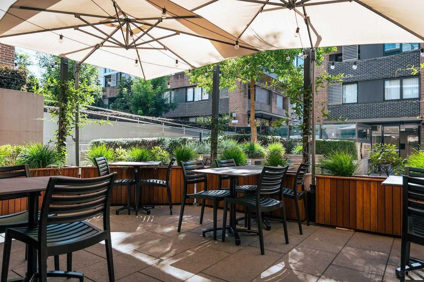 An outdoor event space in a restaurant with wood planters, patio seating, and large umbrellas at Hannah's Beecroft.