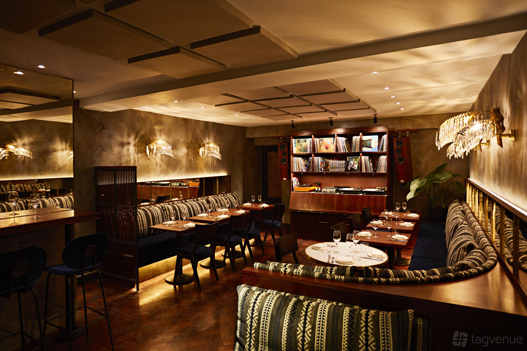 A dining room with patterned banquette seating, wooden tables, and a wall of vinyl records at Caia.