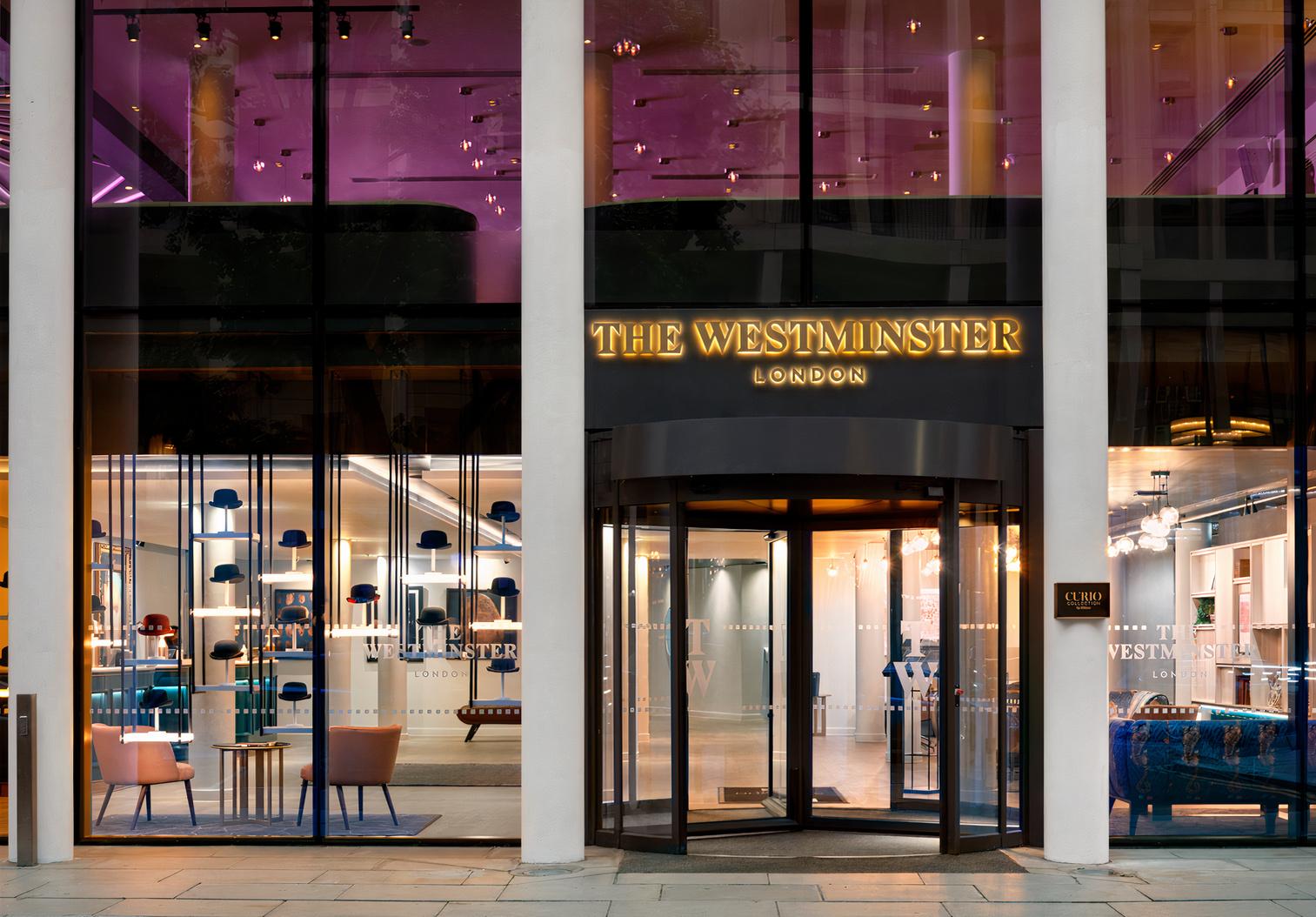 A hotel entrance with a revolving glass door, gold signage, and contemporary lobby seating at The Westminster London.
