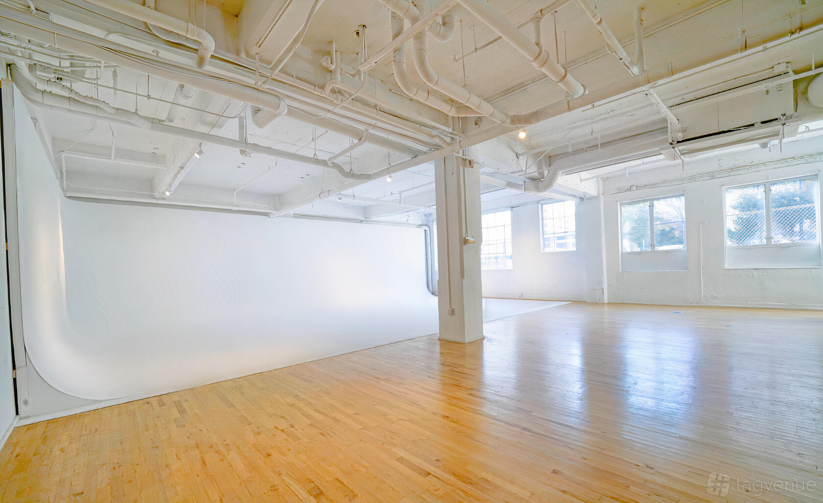 A photo studio with white cyclorama wall, exposed ceiling pipes, and large windows at Studio House Atlanta.