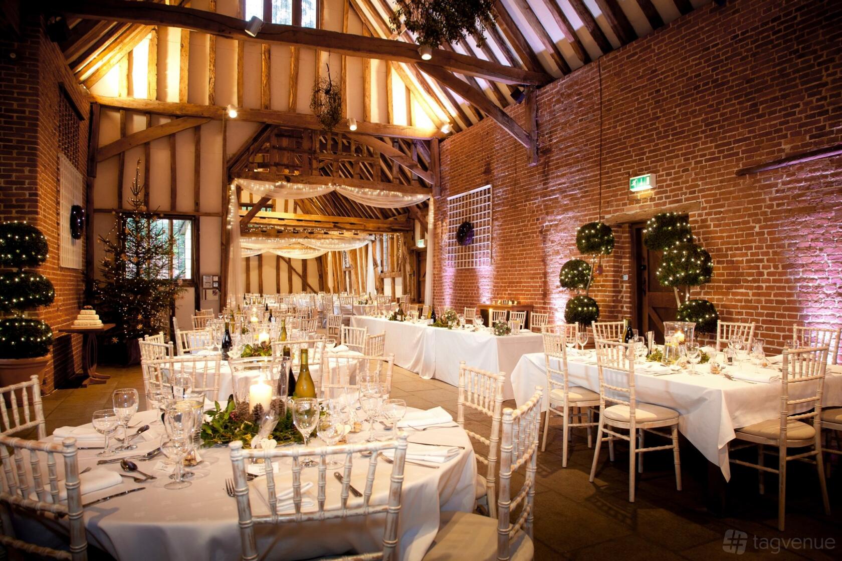 A barn with exposed timber beams, brick walls, and round tables set for dining at Haughley Park.