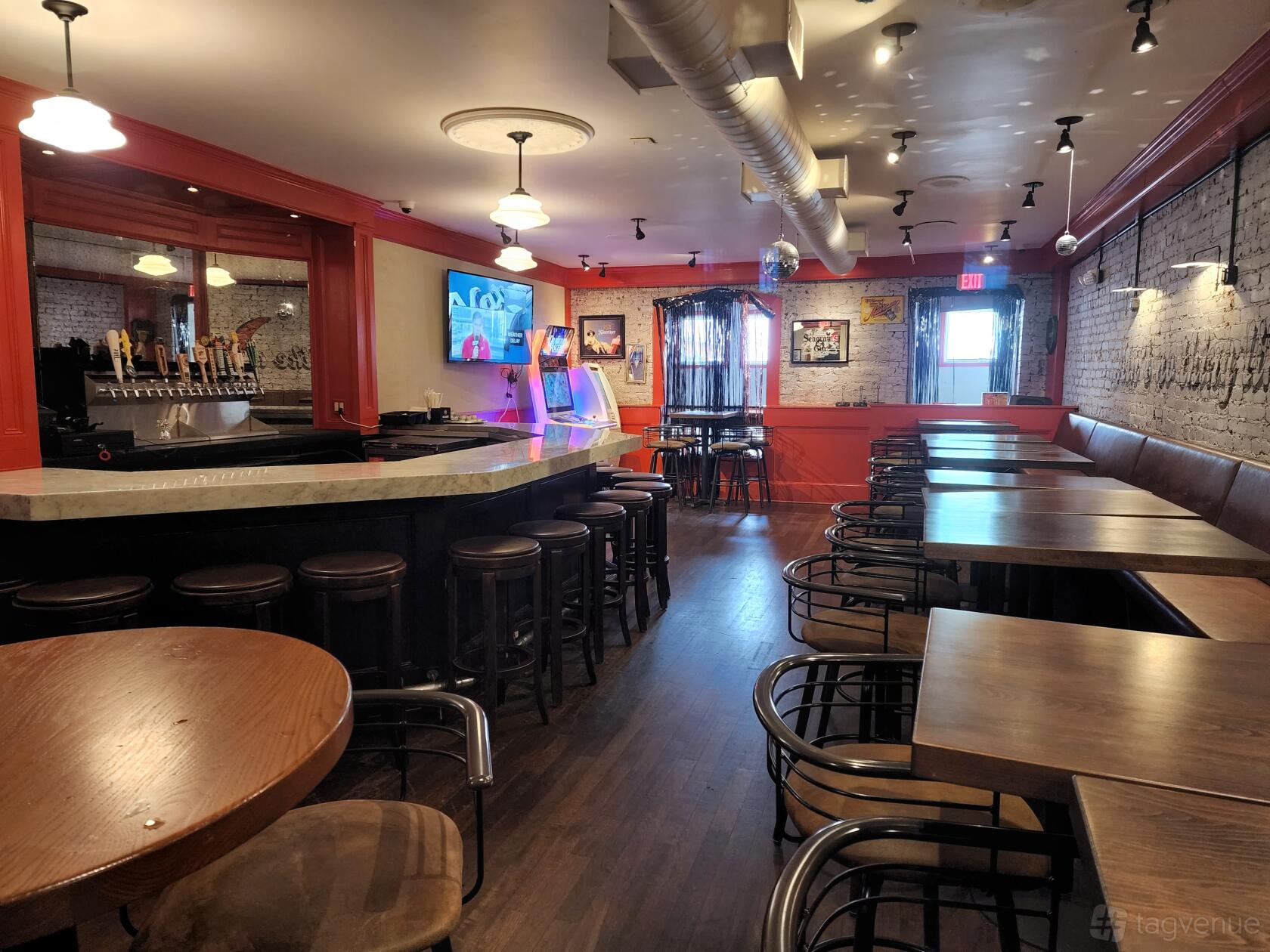 A restaurant with a marble-topped bar, wall-mounted TVs, exposed ductwork, and wooden tables at Wingo's.