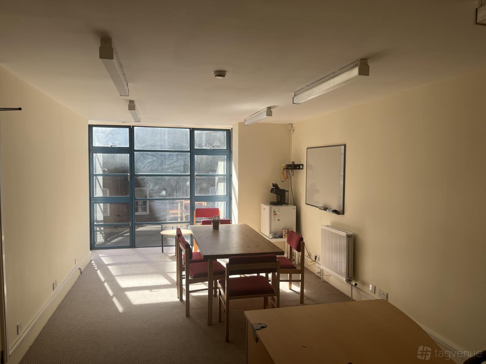 A training room with a large window, rectangular tables, red chairs, and a whiteboard at St Hilda's East.