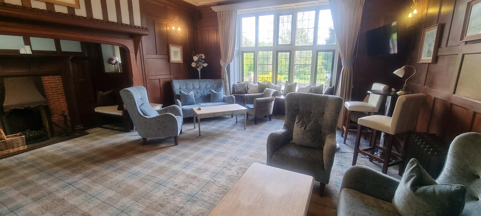 A hotel lounge with upholstered armchairs, a tufted sofa, wood panel walls, and large windows at Farnham House Hotel.