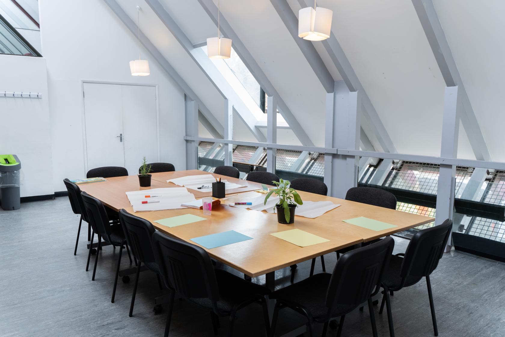 A meeting room with a long rectangular table, black chairs, skylights, and paper supplies at The Albany.