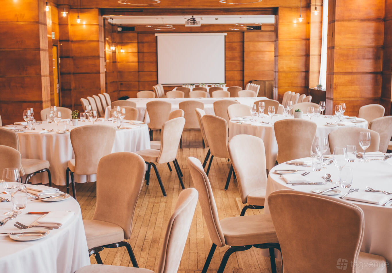 A banquet hall with round tables covered in white linens, beige chairs, and wood-paneled walls at Town Hall Hotel.