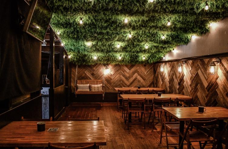 A function room with herringbone wood walls, hanging greenery ceiling, and wooden tables at The River Kitchen & Bar.