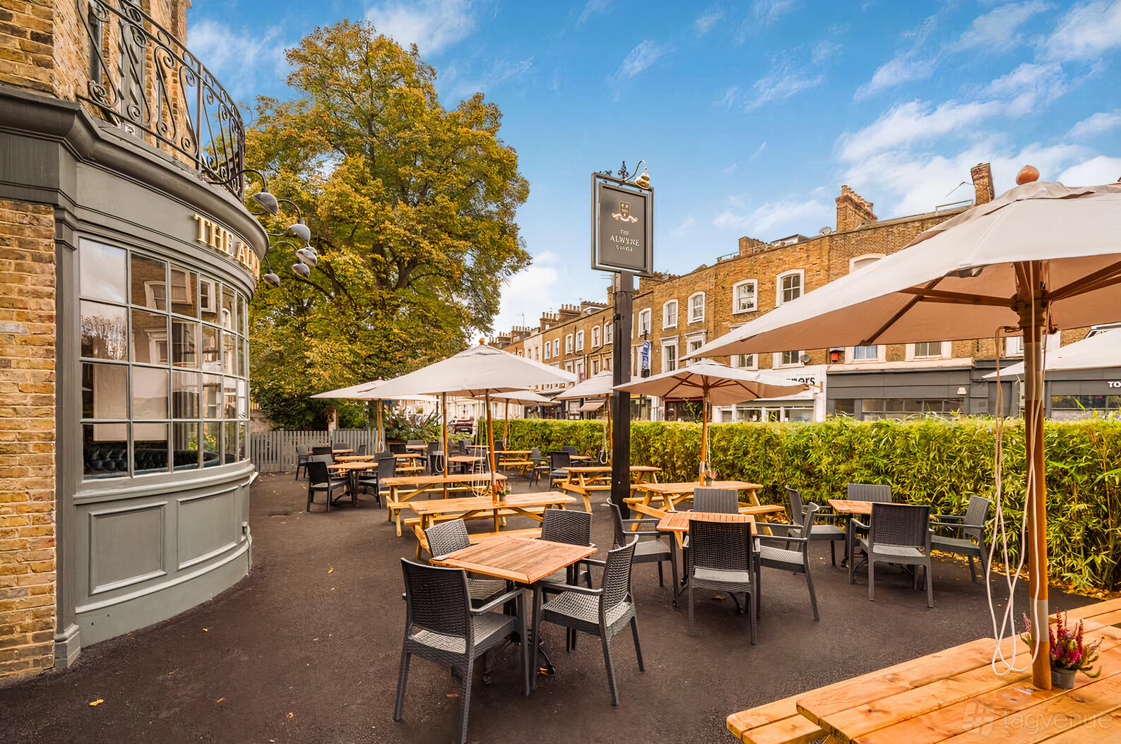 An outdoor pub event space with wooden tables, wicker chairs, and umbrellas at The Alwyne Castle.