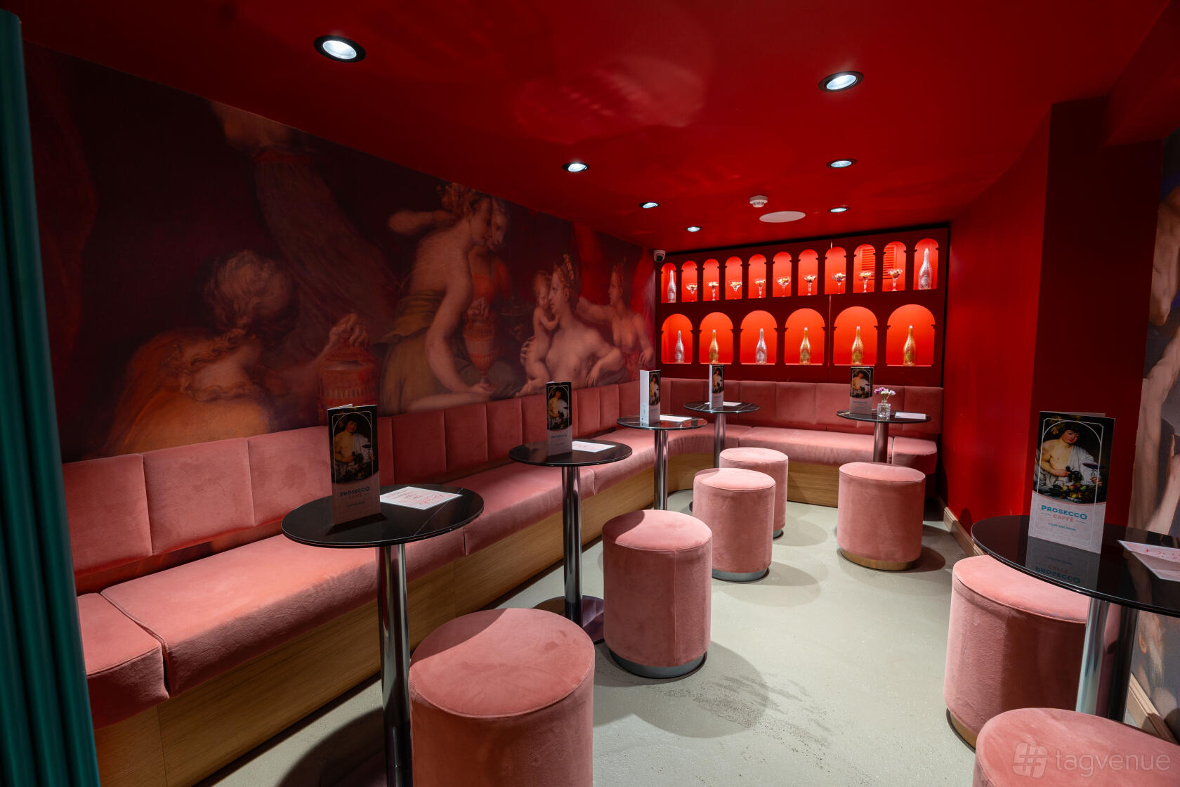 A dining room with red walls, velvet banquette seating, small round tables, and decorative alcove lighting at Prosecco Caffe Soho.