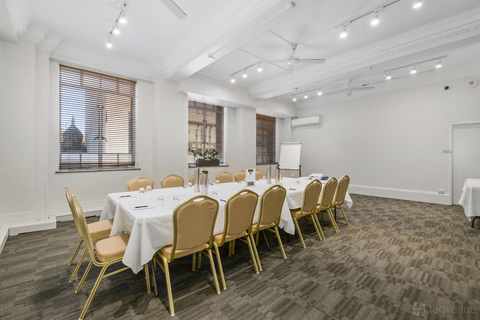 An event space in a hotel with natural light, white walls, and rectangular meeting tables draped in white linens at The Castlereagh Boutique Hotel.