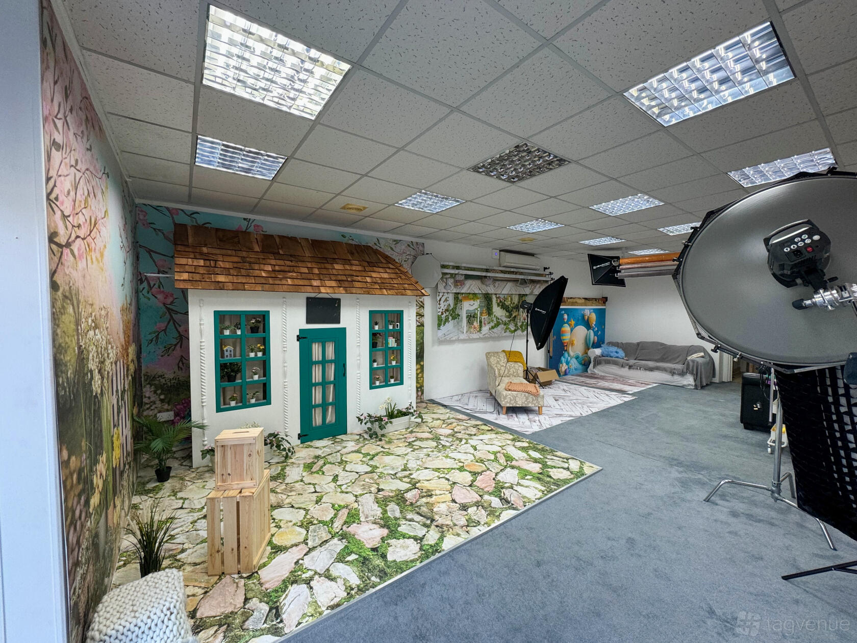 A photo studio with a small cottage set, printed backdrops, and professional lighting equipment at Frame Studio.
