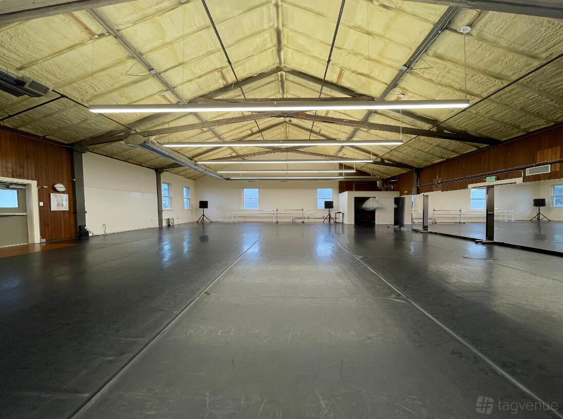 A dance studio with a high exposed beam ceiling, wall mirrors, ballet barres, and large windows at Moving Arts Academy of Dance.