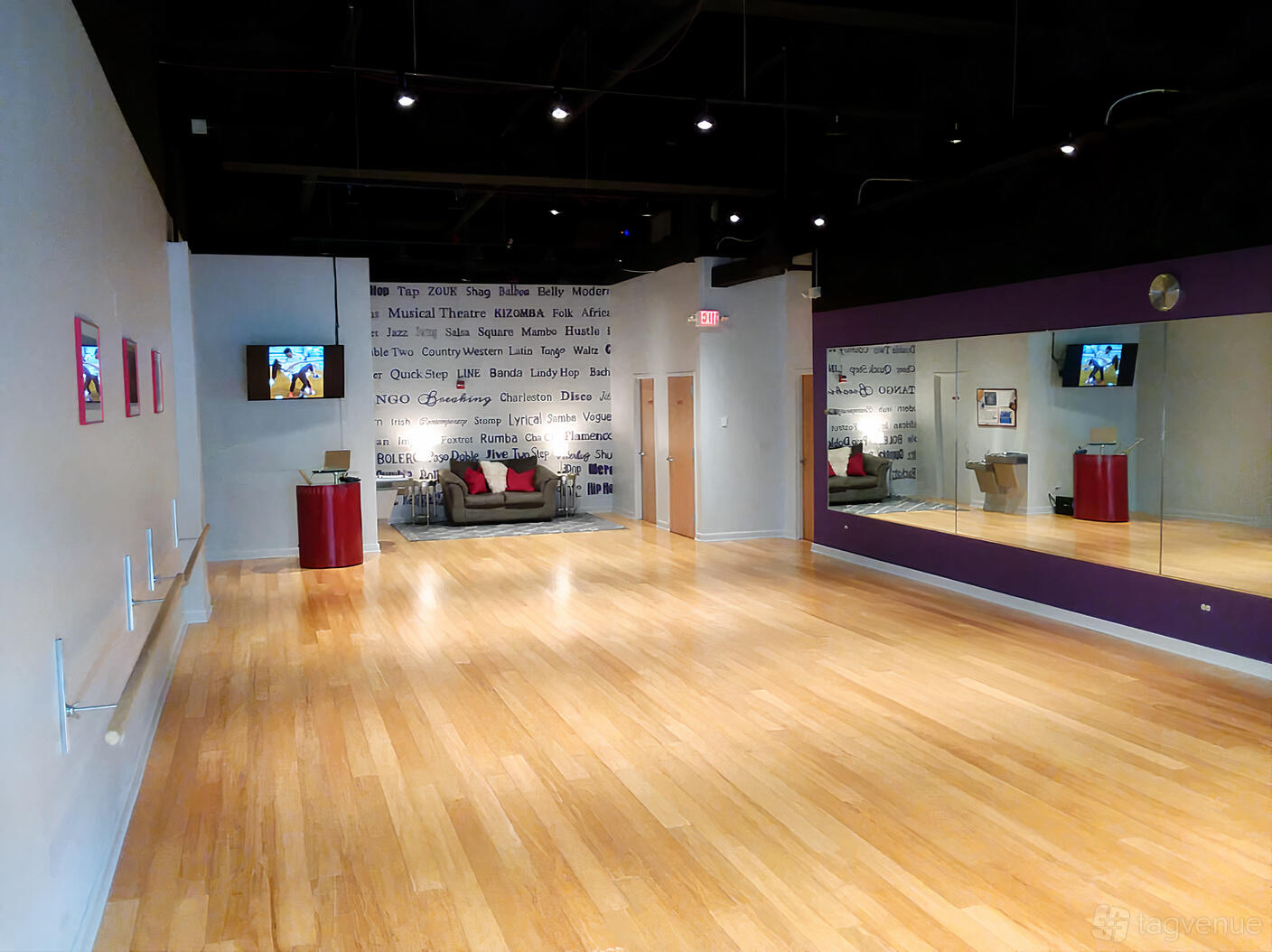 A dance studio with wood floors, full-length wall mirror, ballet barres, and a sofa seating area at Move the Beat.