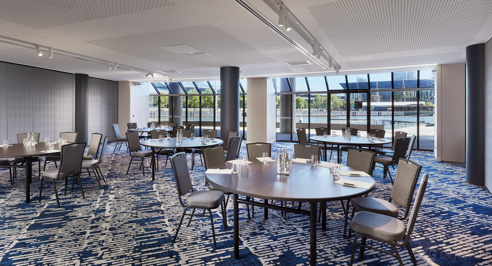 A meeting room with round tables set with water glasses and notepads, floor-to-ceiling windows at Pearl Riverfront