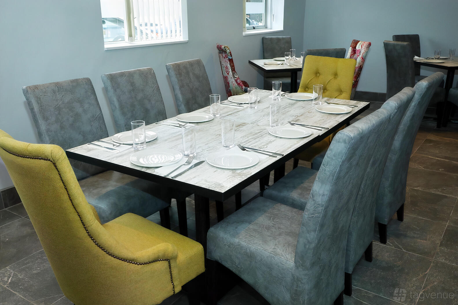 An event space in a restaurant with a long wooden table, gray and yellow chairs, and table settings at Takaa Tak, Oldbury.