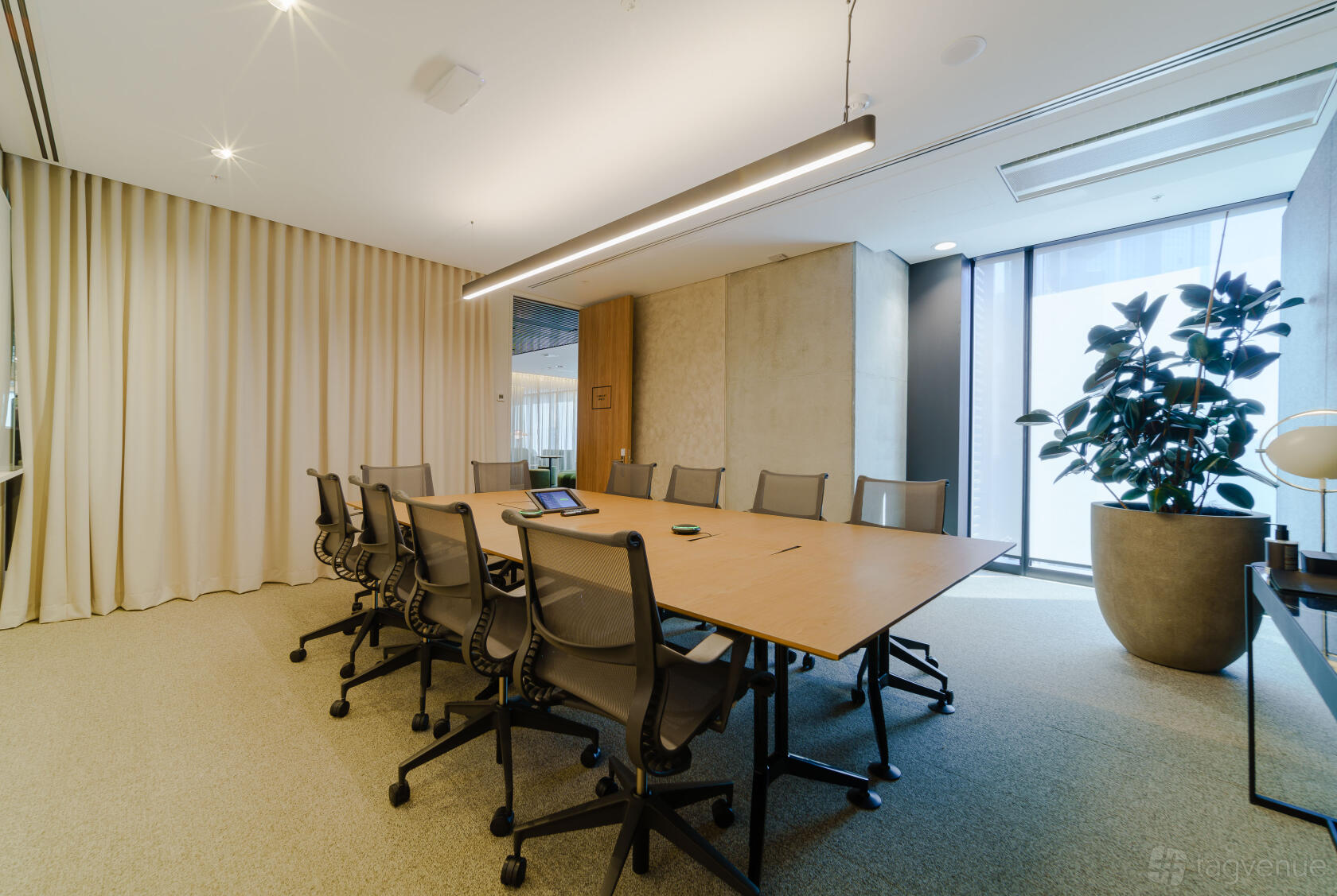 A coworking space with a long conference table, mesh office chairs, floor-to-ceiling window, and indoor plant at Hub Wynyard.