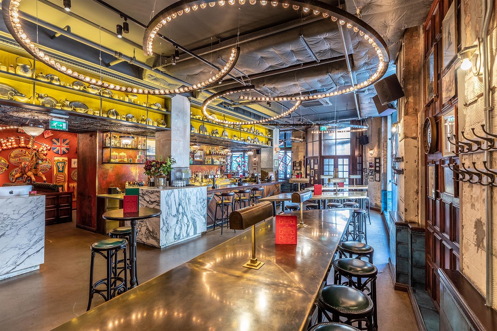 An event space with circular pendant lights, marble bar counters, and high tables with stools at Flight Club Leeds.