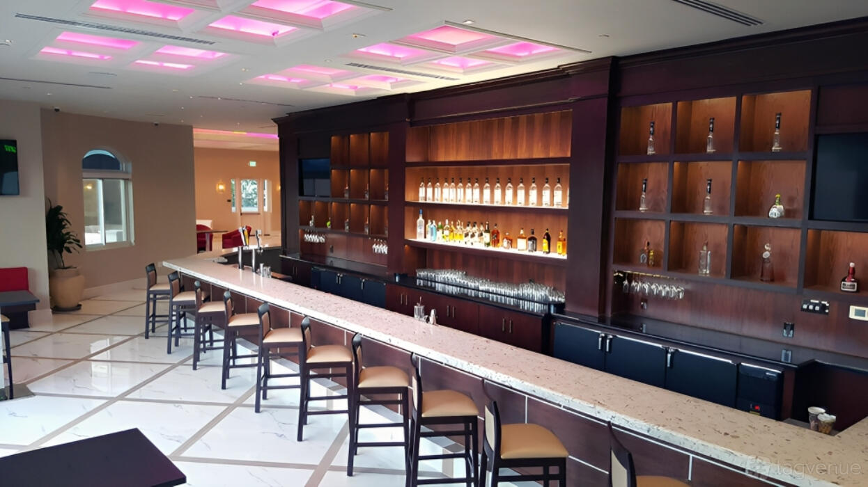 A fitness studio bar with a long marble counter, high-back chairs, and backlit shelves of bottles at South End Racquet And Health Club.