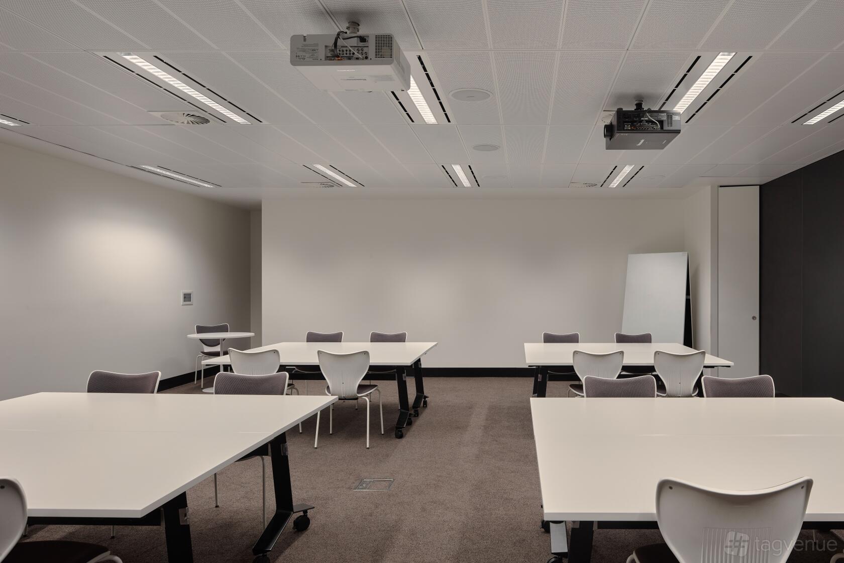 A meeting room with white tables, gray chairs, ceiling projectors, and a whiteboard at Flex by ISPT at 4 National Circuit.