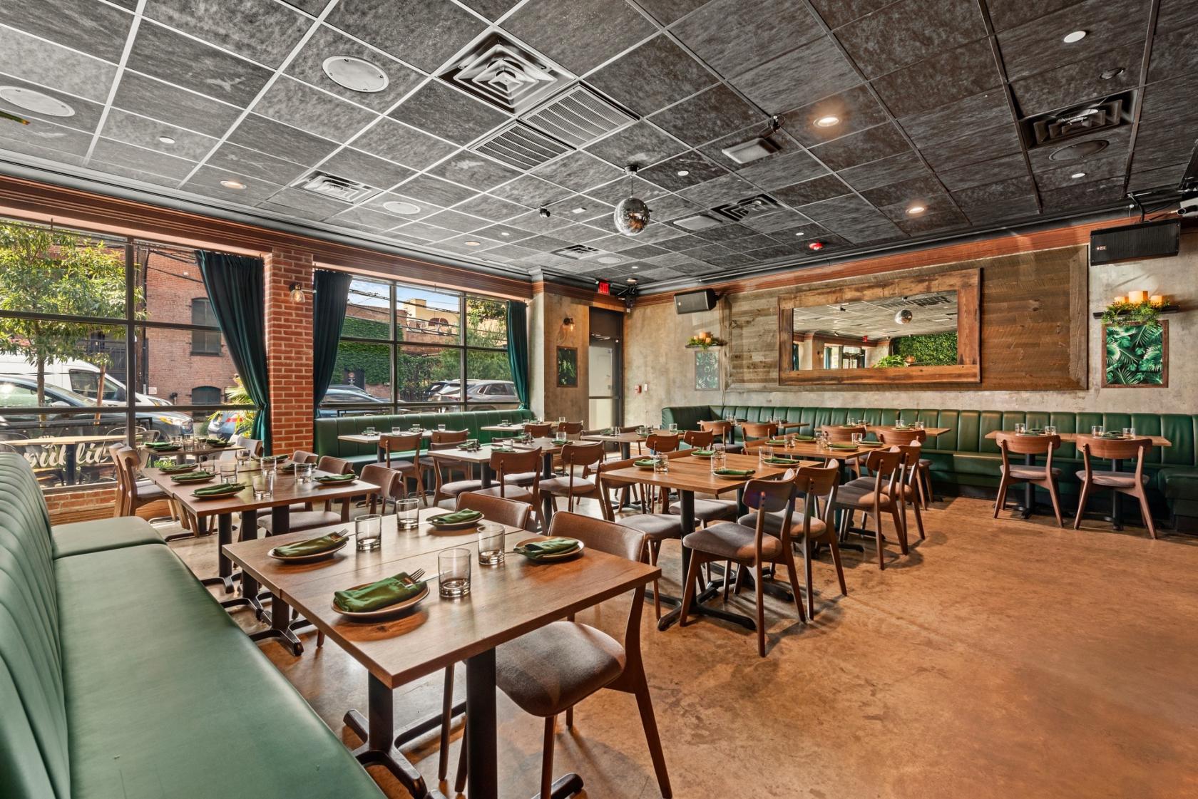 An event space with green leather banquette seating, wooden tables, and large windows at Republic Latin Fusion.