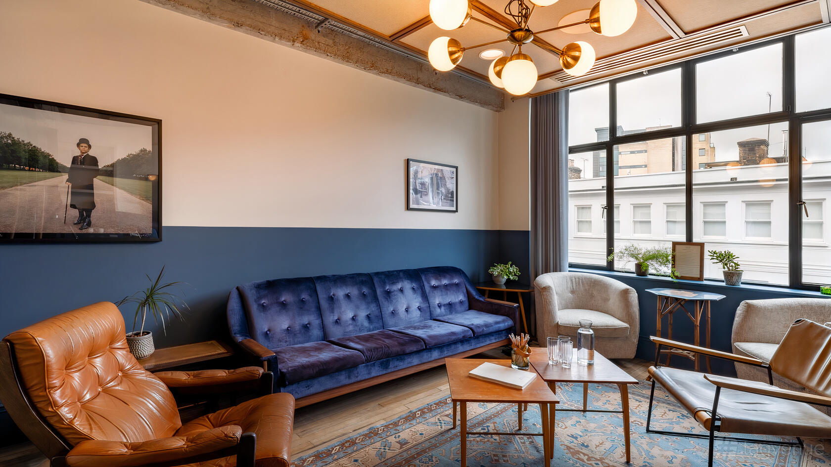 A bar lounge with a velvet sofa, leather armchairs, patterned rug, and large window at Mortimer House.