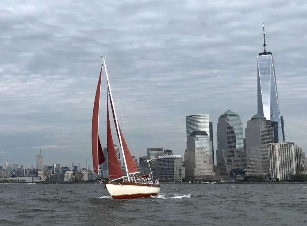 A yacht with red sails cruising on the water with Manhattan skyscrapers in the background at Narwhal Yacht Charters.