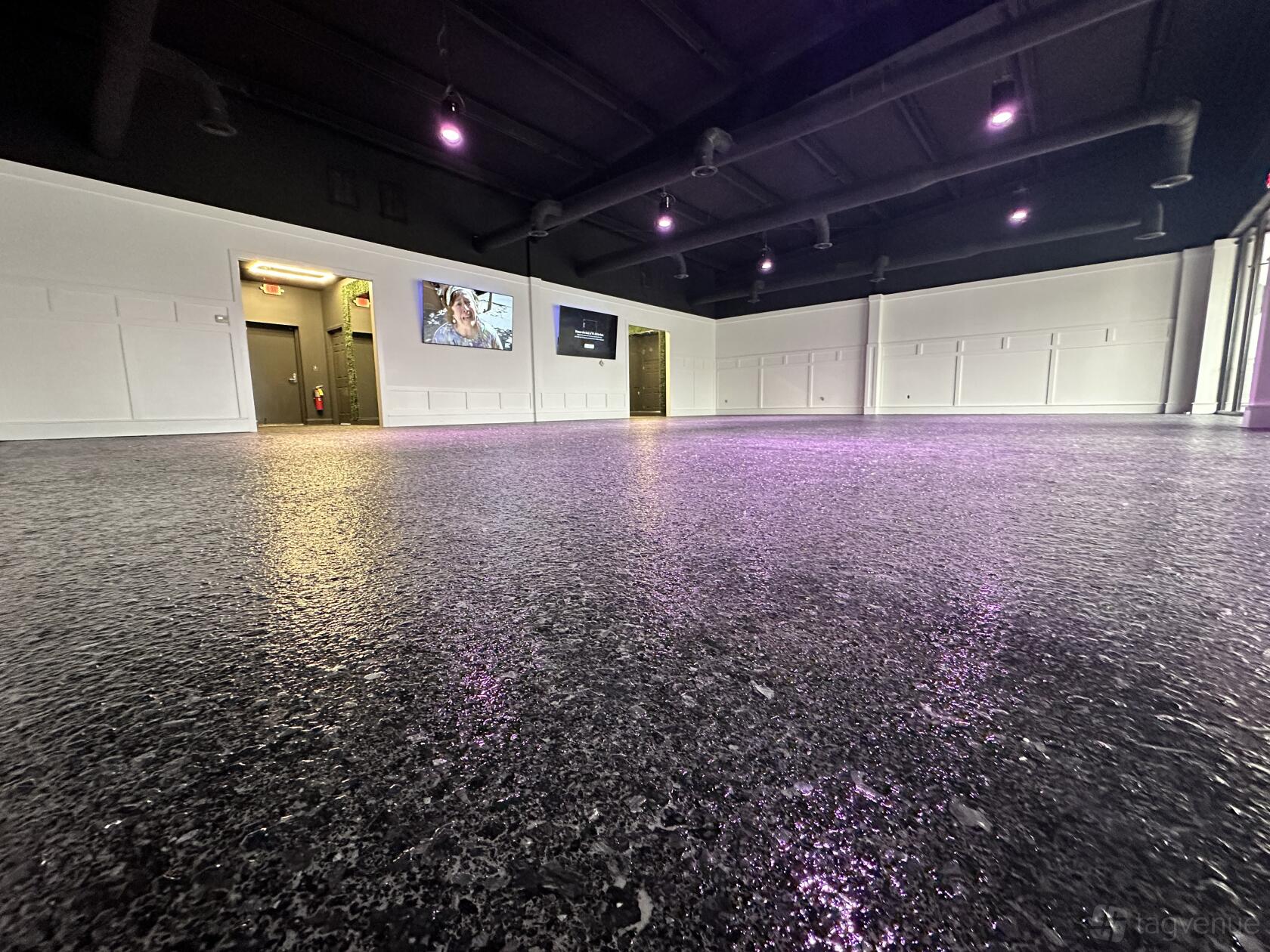 An event venue with polished concrete floors, white paneled walls, and purple ceiling lights at Spec Events.