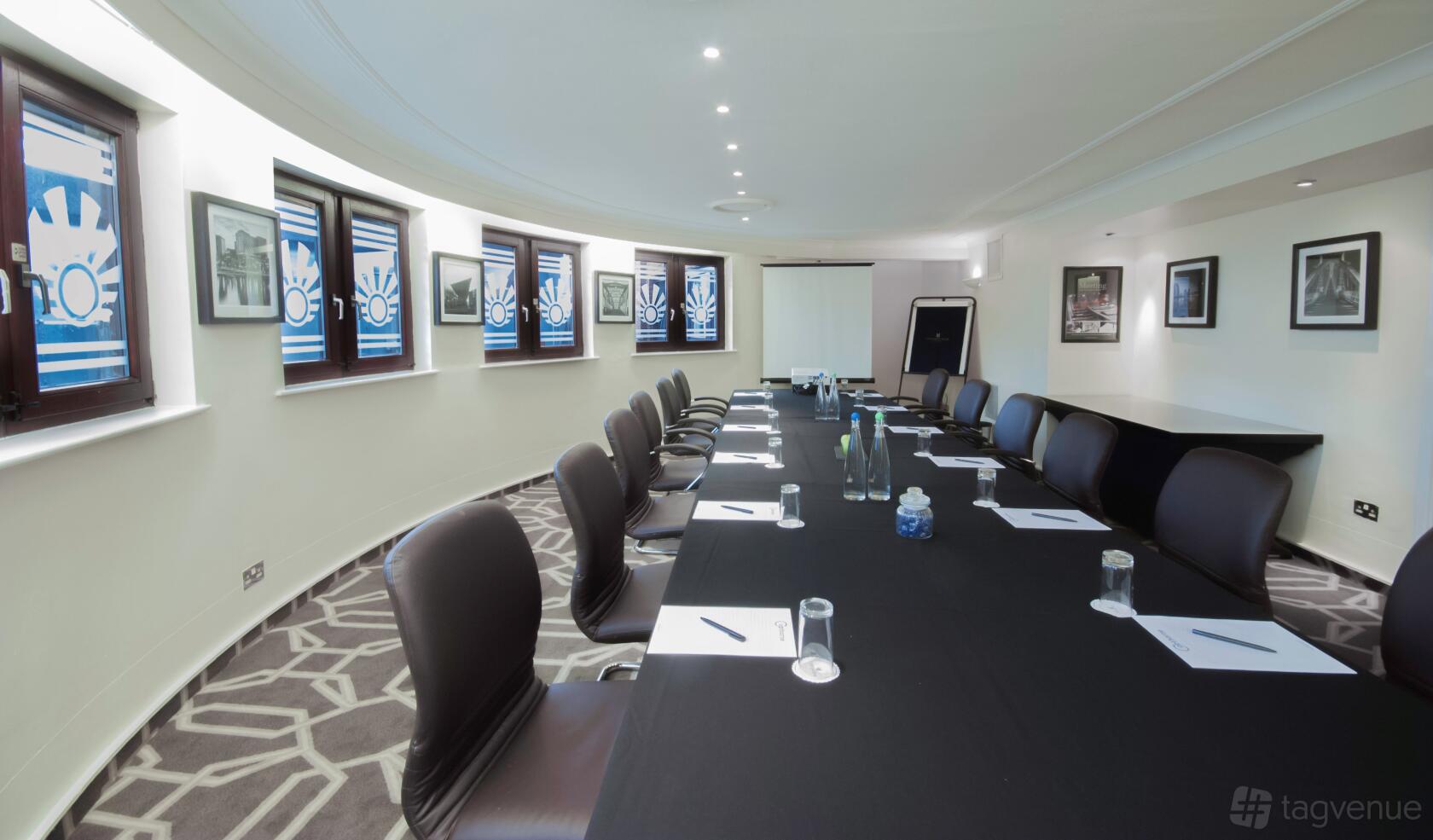 A hotel meeting room with a long boardroom table, black chairs, and large windows in the McCallum Suite at Copthorne Hotel Manchester.