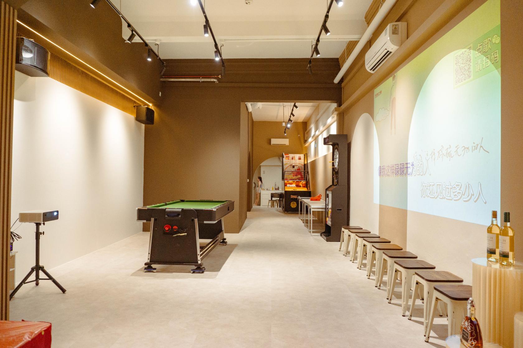 An event venue with a pool table, projector screen, and rows of stools along one wall at Space99.
