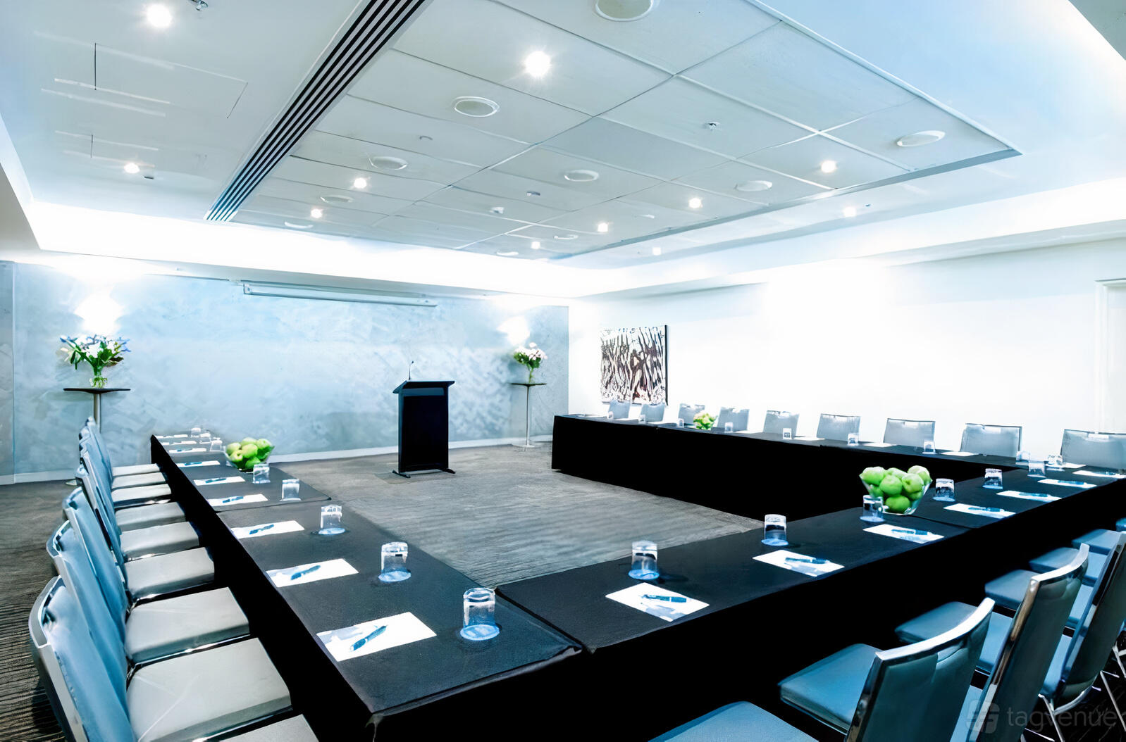 A hotel meeting room with U-shaped tables, padded chairs, notepads, water glasses, and decorative flowers at Mantra Chatswood.