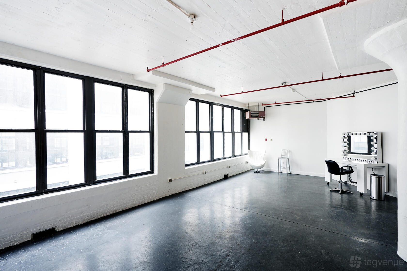 A photo studio with large industrial windows, black flooring, and a makeup station at Plum Studio.