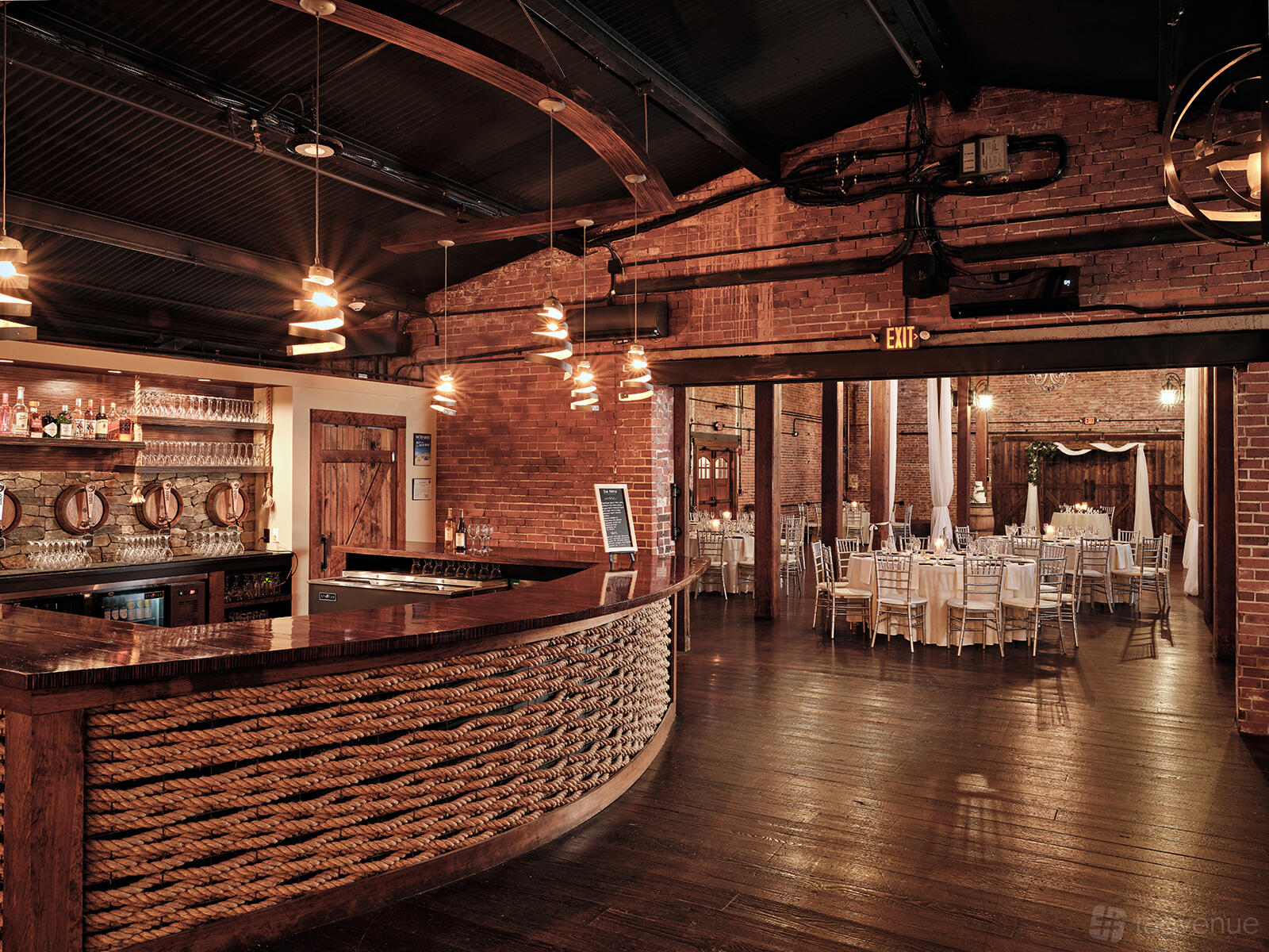 An event venue with a wooden bar wrapped in rope, exposed brick walls, and hanging pendant lights at 1620 Winery.