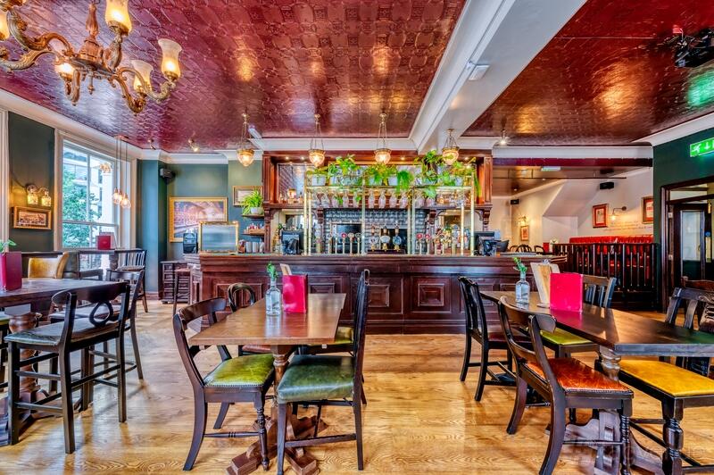 An event space in a pub with wooden tables, mixed chairs, and a decorative bar lined with plants at The Globe.
