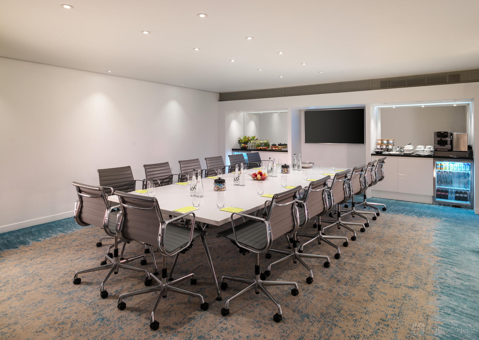 A hotel boardroom with a long white table, ergonomic chairs, wall-mounted screen, and refreshment station at St Martins Lane London.